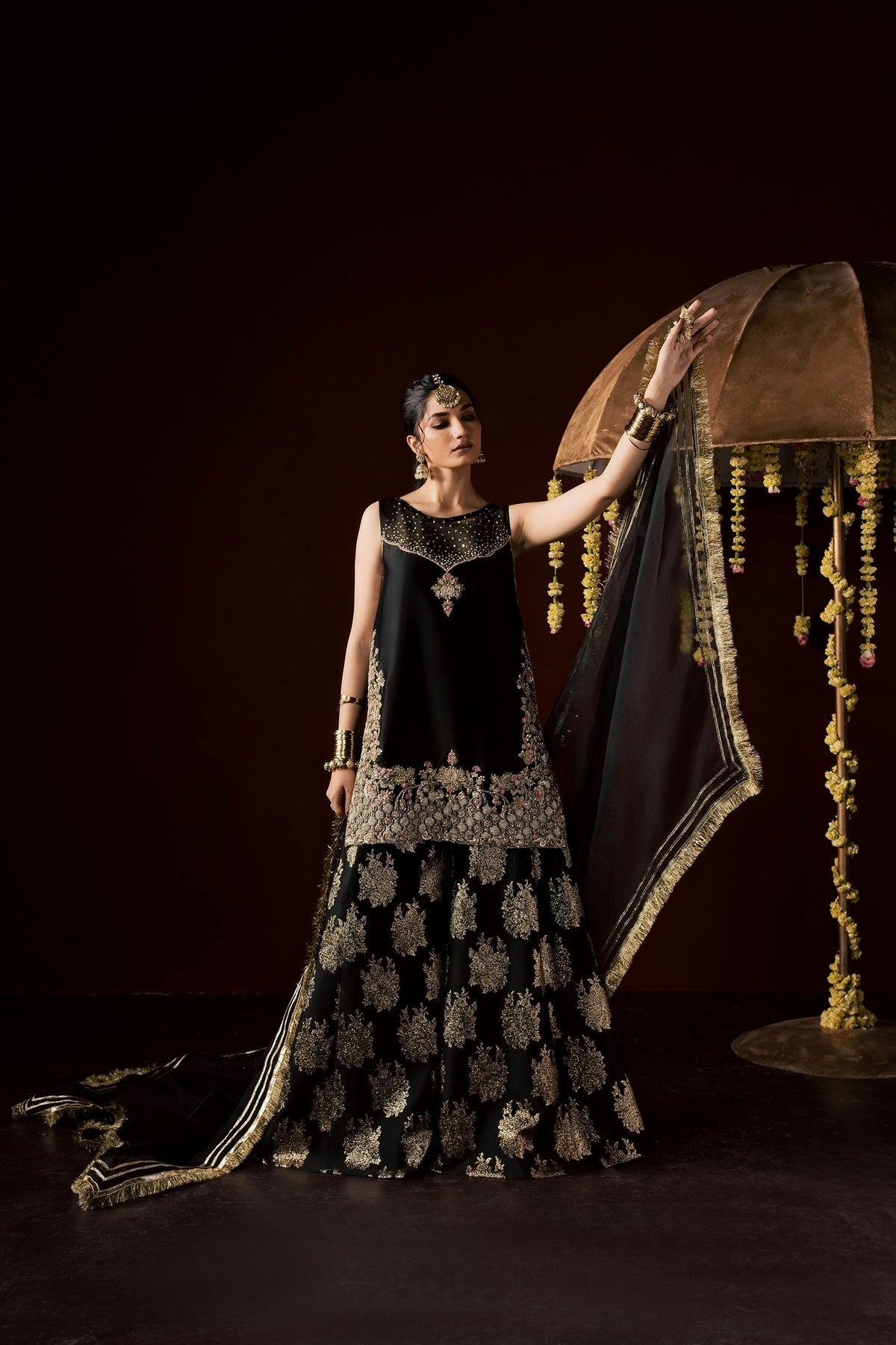 Zonaira Ahmed Laila black gold wedding formal 3-piece – full-length front view with hand on decorative canopy prop