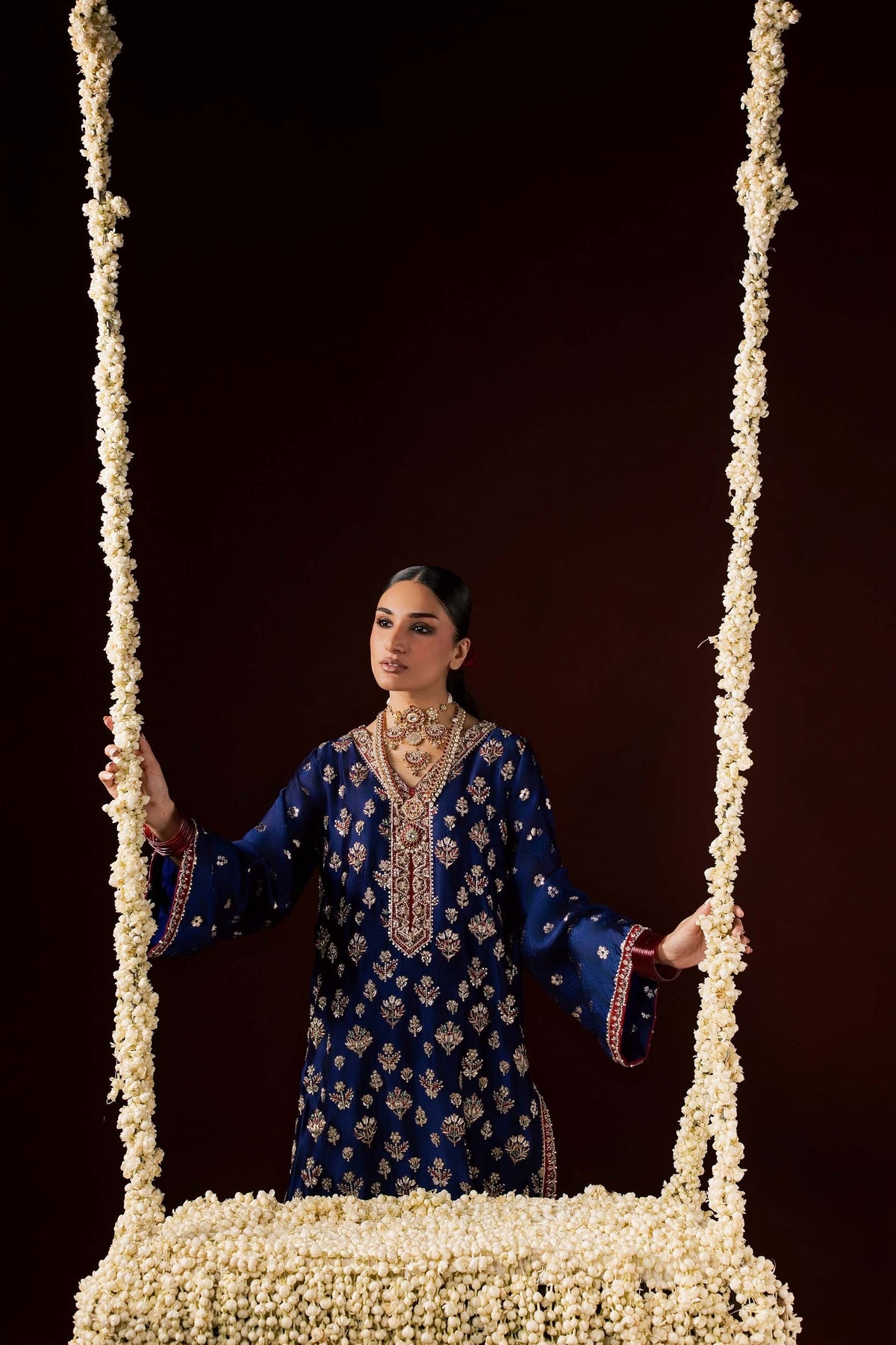 Zonaira Ahmed Nayab navy blue wedding formal 3-piece – front view standing on a floral swing, showcasing the sheesha silk kurta and shalwar embroidery