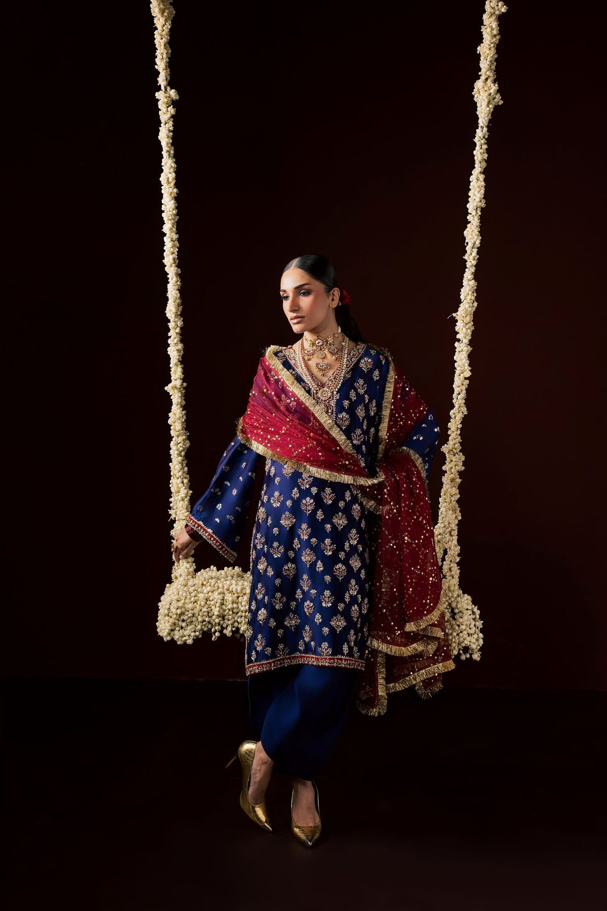 Zonaira Ahmed Nayab navy blue wedding formal 3-piece – full-length view with red dupatta draped diagonally, standing on a swing