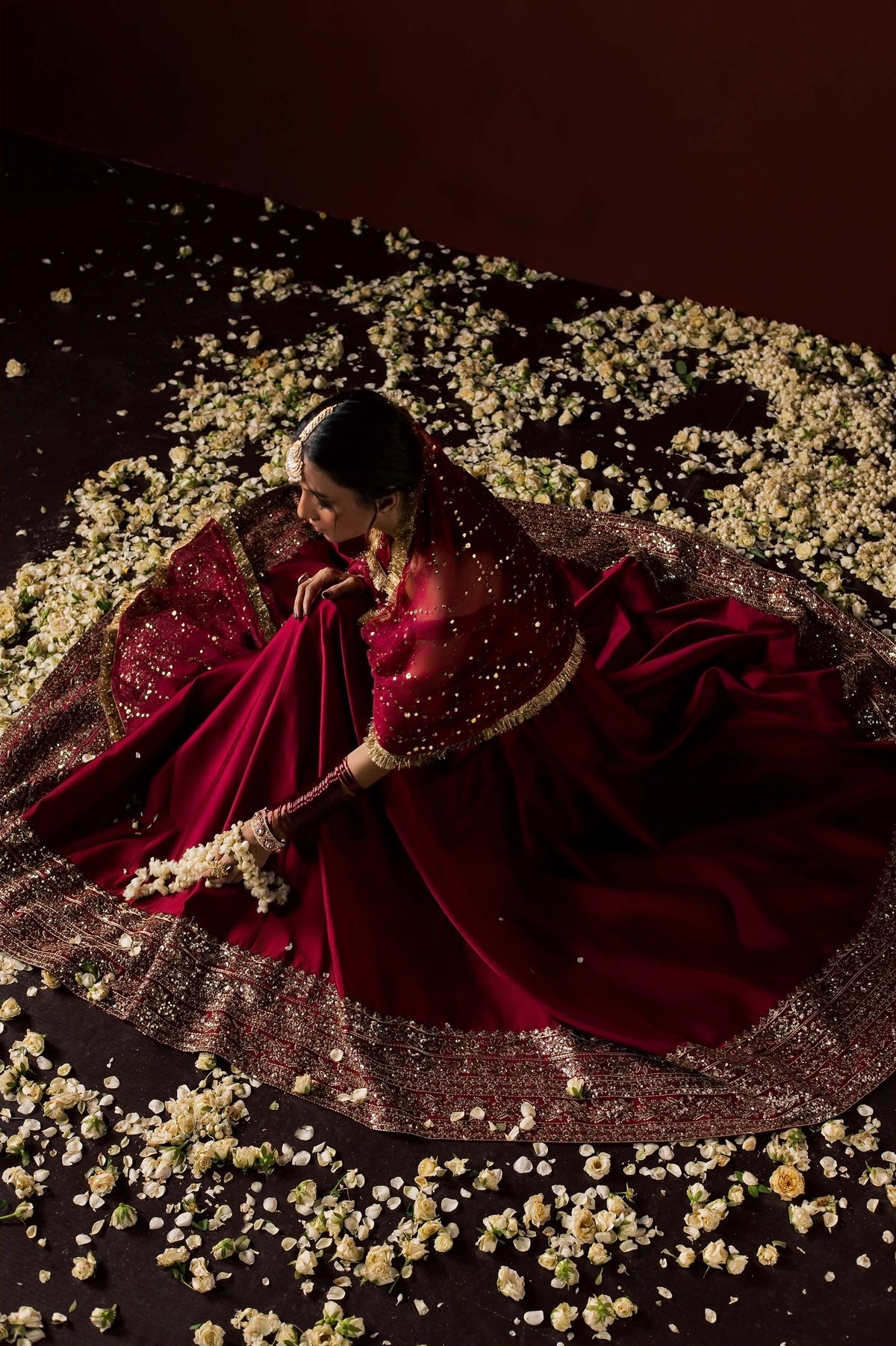 Zonaira Ahmed Neysa maroon wedding formal peshwas – overhead view of the gown fanned out among flower petals, showcasing the richly embellished border
