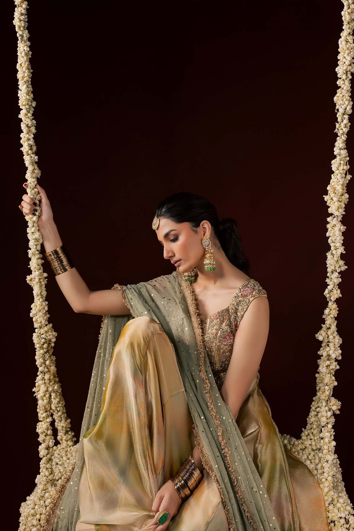 Zonaira Ahmed Nooré gold ombre wedding formal 3-piece – seated on a floral swing, holding the garland rope