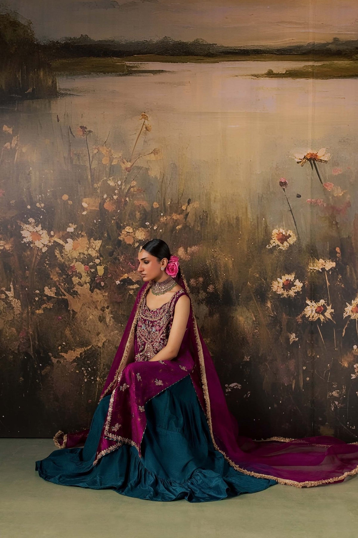 Zonaira Ahmed Rania magenta teal wedding formal 3-piece – seated pose with teal skirt fanned out, painted floral lake backdrop